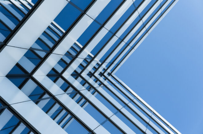 Modern glass office building viewed from below against a blue sky.