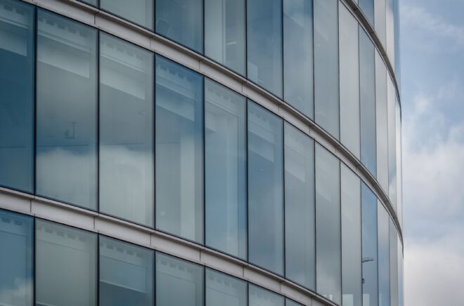 Curved glass facade of a modern London office building reflecting the sky.