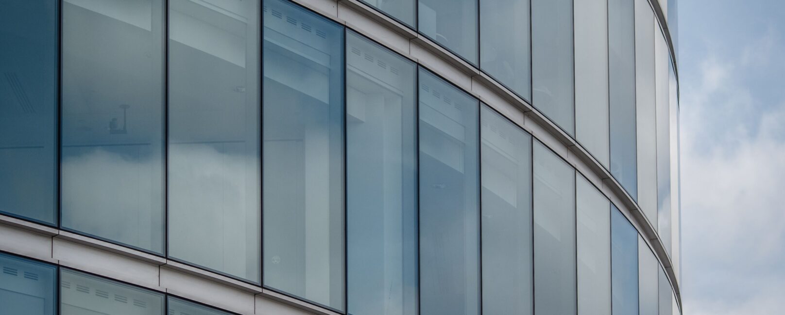 Curved glass facade of a modern London office building reflecting the sky.