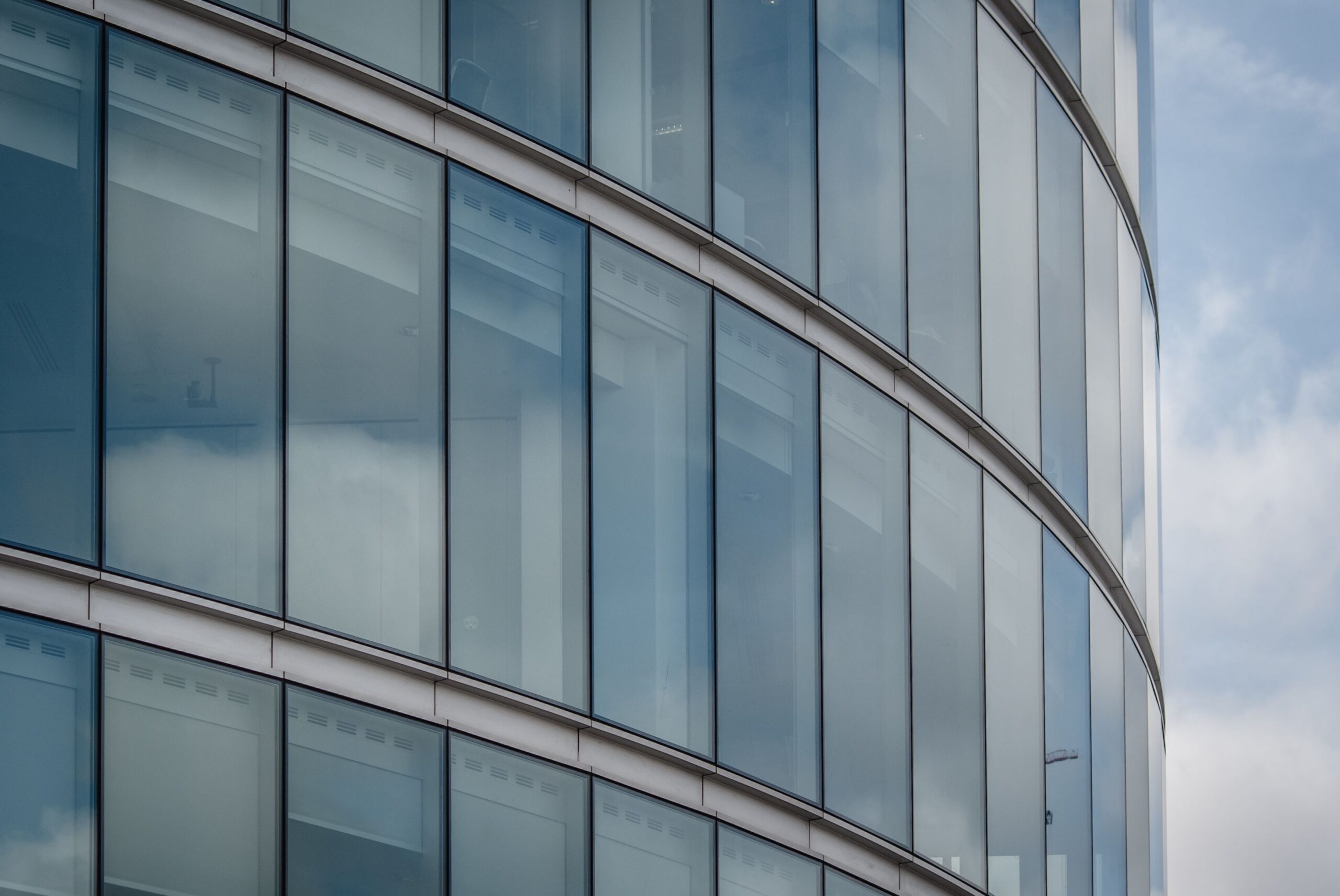 Curved glass facade of a modern London office building reflecting the sky.