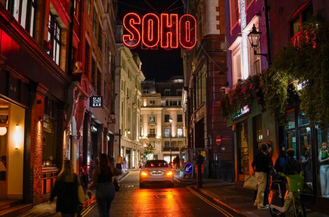 Illuminated Soho sign above a London street at night